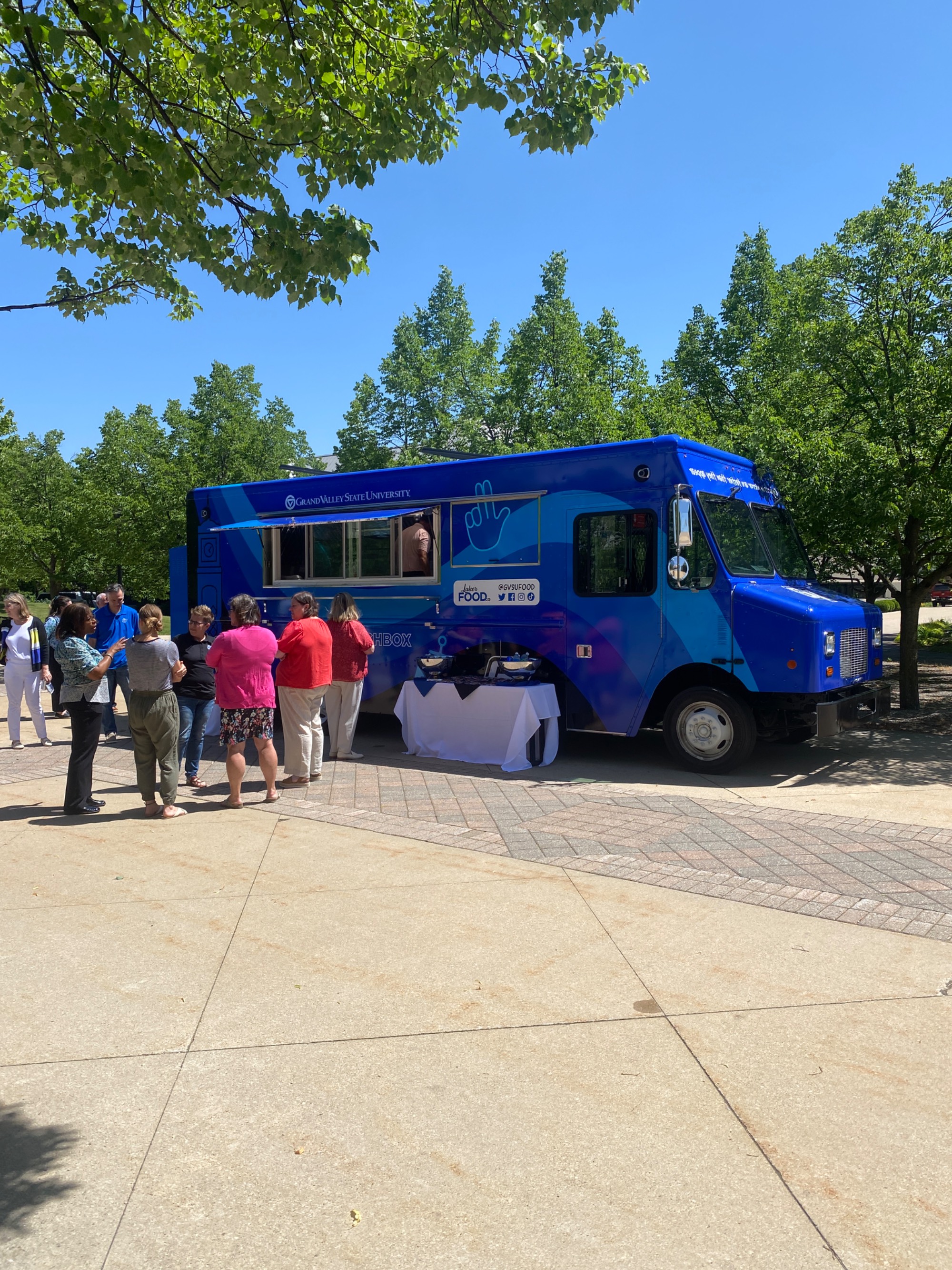 group of people standing next to Louie's Lunchbox food truck on GVSU's campus